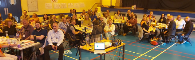 Picture of a group of CLD workers in a community centre sat at tables of 8 and all smiling