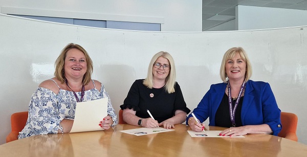 Dr Marion Allison, Allana Mullen and Kirsty Gemmell sitting  at a table signing document.